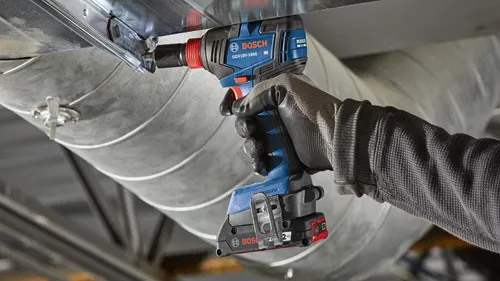 Bosch GDX18V-1800 cordless impact driver being used to tighten a screw on metal ductwork.
