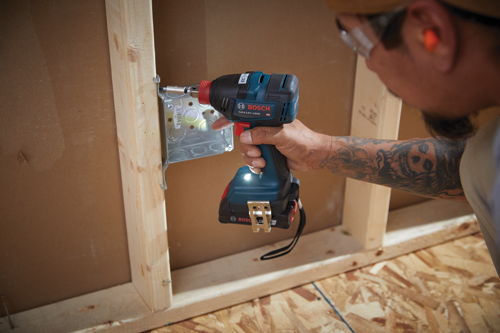 Bosch GDX18V-1800 HD impact driver being used to attach a metal bracket to a wall stud; a person holds the tool.