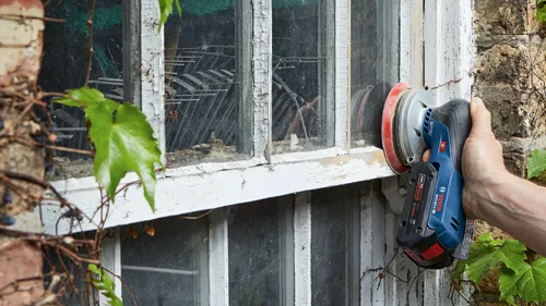 Bosch GEX18V-5 sander, with "AMP Share!" battery, sanding a window frame.