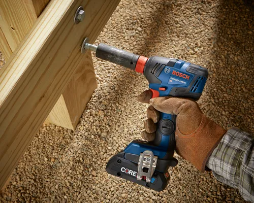 Bosch GDX18V-1800C HD impact driver being used to tighten a bolt on a wooden structure, held by a person wearing a brown work glove.