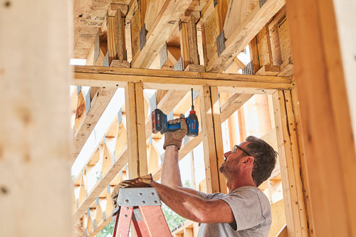 Man with a Bosch cordless impact driver drilling in wood frame.