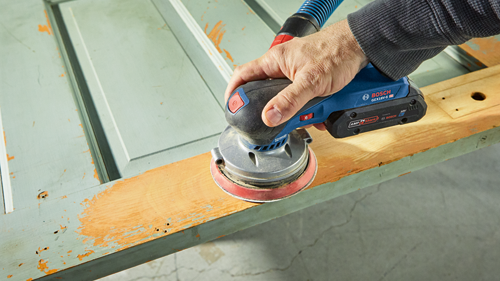 Man using the Bosch cordless sander connected to a vacuum hose sanding a door.