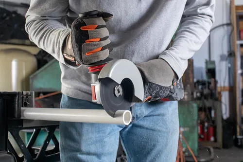 Person wearing protective gloves using an angle grinder to cut a pipe.