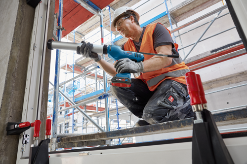 Person using Bosch GCU18V-30 caulking gun; wearing gloves, safety glasses, a hard hat, and an orange vest.