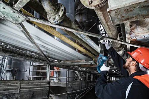 Person using a Bosch reciprocating saw in an industrial setting, wearing safety gear.