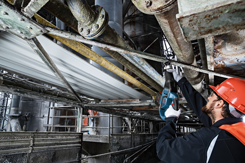 Person using a Bosch reciprocating saw in an industrial setting, wearing safety gear.