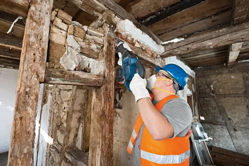 A person wearing safety gear using a Bosch reciprocating saw to cut an overhead beam.