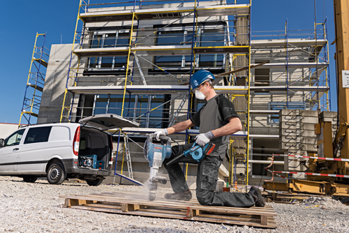 Man wearing safety gear uses a Bosch demolition hammer and blower on a construction site.