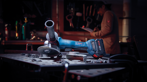 Bosch GWS18V-10P angle grinder, with CORE18V 8.0 Ah battery, on a metal table; a person is in the blurred background.