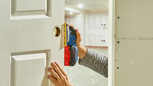 Bosch GSS18V-40 18V brushless orbital sander being used to enlarge a door knob hole on a white door.
