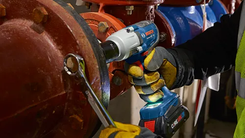 Bosch GDS18V-330PC impact wrench being used with a wrench, against red and blue pipes. The wrench is being used with CORE18V 4Ah battery.