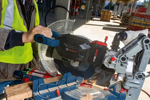 Bosch electric miter saw, a person holding the handle, wearing a yellow safety vest, and the battery shows "AMP Share 18V Powered by BOSCH 12Ah".