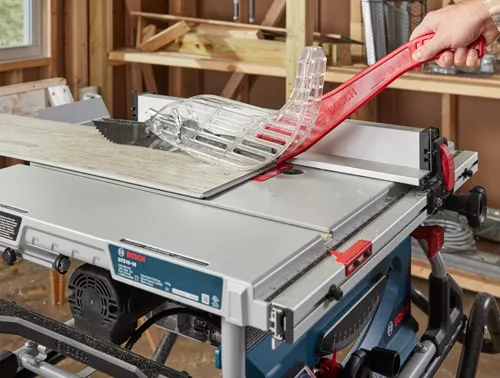 Bosch GTS15-10 table saw with safety guard, cutting a piece of wood.