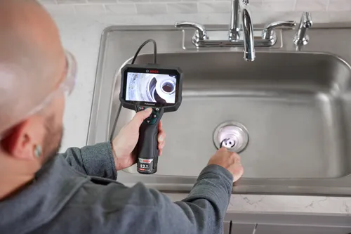 Bosch Professional inspection camera in use. The screen displays the interior of a drain.
