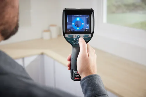 Bosch thermal imaging camera held by person, displaying "Cold Detector," with temperatures "77.5°F" and "68.5°F", and a "12 MA 2.0 Ah Li-Io" battery.