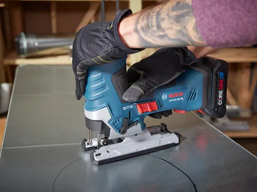 Bosch GST18V-50B HD jigsaw is cutting a circular line in a metal sheet, held by a person wearing black gloves.