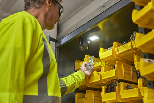 Person holding screws near yellow storage bins, with light and shelves visible.