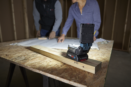 Bosch CORE18V 4Ah work light on a wooden beam, people working on blueprints in the background.