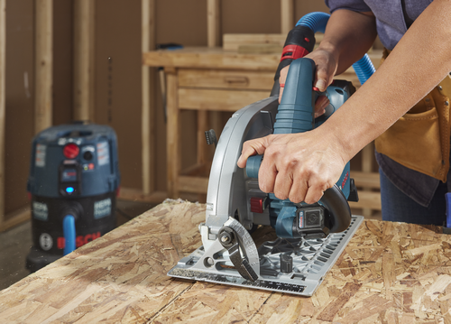 Bosch circular saw cutting wood on a workbench. A shop vacuum is visible in the background.