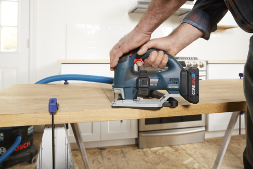 Bosch jigsaw cutting wood, hands of a person holding it, blue and black color