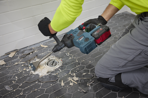 Bosch 18V Hammer Drill, a person kneels with a Bosch tool to remove tiles from a floor. The drill is powered by an "AMP Share" 18V 6.0 Ah battery.