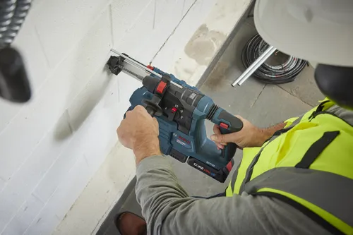 Bosch GBH18V-22 rotary hammer drill, CORE18V battery, drilling into a wall; person wears safety vest and hard hat.