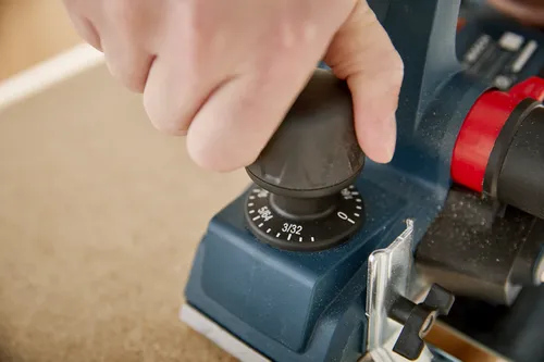A hand turning a black dial on a teal power tool, with '3/32' and measurements visible.