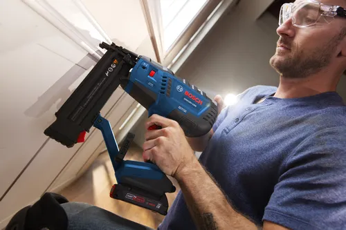 Bosch GNH18V-18M 18-GA BRUSHLESS MOTOR nailer being used by a person wearing safety glasses. The tool features “18ga Nail Capacity/Capacité du Clou/Capacidad de Clavos 5/8-2-1/8 in. (15-54 mm) (L)”