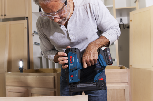 A person wearing safety glasses holds a Bosch GTH18V-18M nailer.