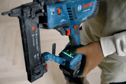 Bosch GTH18V-18M nailer in use, held by a person wearing a brown work glove.