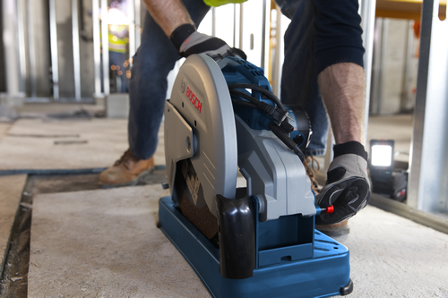 Bosch electric cut-off saw with "BOSCH" logo, being operated by a person wearing work gloves.