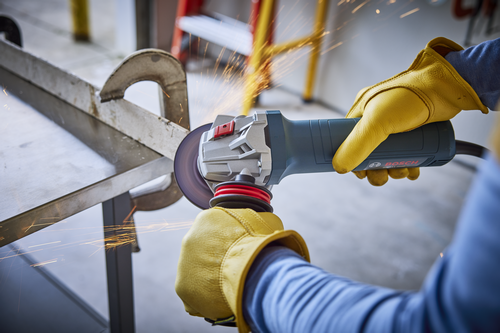 Bosch angle grinder in use, held by a person wearing yellow gloves, sparks flying.