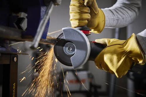 Person wearing yellow gloves operating an angle grinder, with sparks flying. A metal pipe is held in a vise.