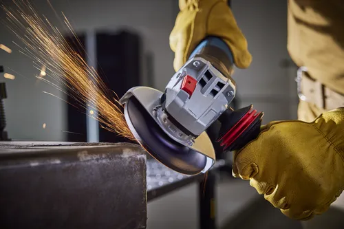 Person wearing yellow gloves using an angle grinder, with sparks flying from the blade.