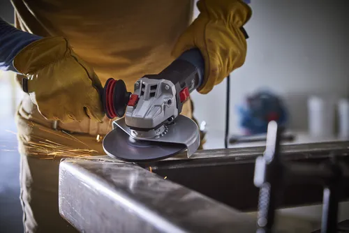 Person using an angle grinder, sparks flying as it cuts metal.