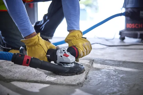 A person wearing gloves using a grinder near a BOSCH vacuum cleaner.
