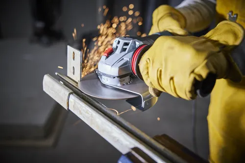 Person wearing yellow gloves using an angle grinder, with sparks flying from the blade while cutting a metal bar.