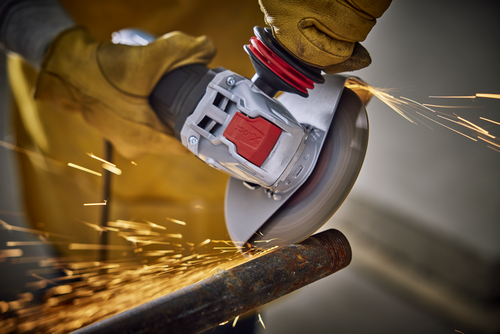 A person wearing a yellow glove uses a grinder tool on a metal pipe, generating sparks and "X-LOCK".