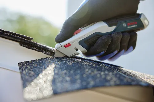 A person using the Bosch H11-13000-1 Retractable knife cutting a roofing material.