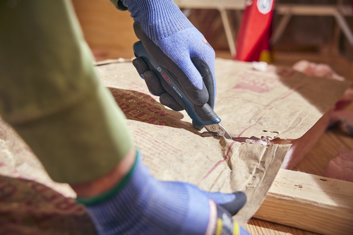 A person using the Bosch H11-12100-1 snap off knife cutting a cardboard layer.