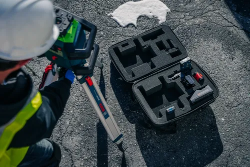 Bosch BT 150 HD tripod, person wearing hard hat using Bosch measuring device, and opened case with tools.
