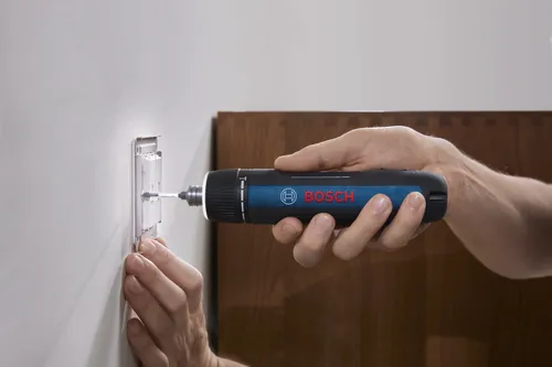 A profile view of someone using the Bosch GSD4V-35 rechargeable screwdriver to install a lightswitch on a wall.