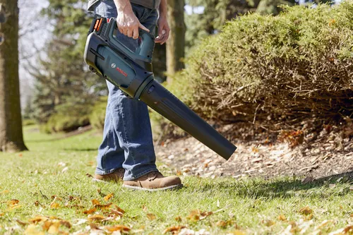A worker using the Bosch GBL18V-450N PROFACTOR™ 18V Blower to blow the dry leaf from the garden.