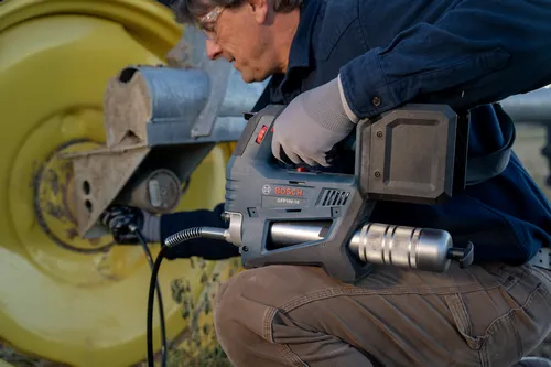 A worker using the Bosch GFP18V-10 18V Grease Gun on a vehicle wheel.