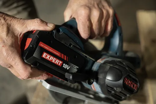 A worker attaching a Bosch EXBA18V-60 EXPERT 18V 6 Ah High Power Battery to a power tool.