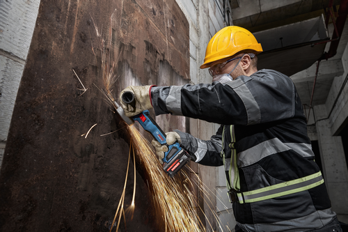 A worker grinding metal on a wall with the Bosch 18V Brushless 4-1/2 – 5 In. Angle Grinder with Slide Switch.