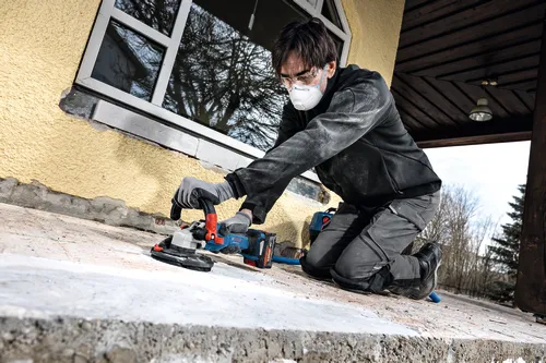 Image of worker using the Bosch GBR18V-15S 5 In. 18V Concrete Surface Grinder to grind a hard concrete floor.
