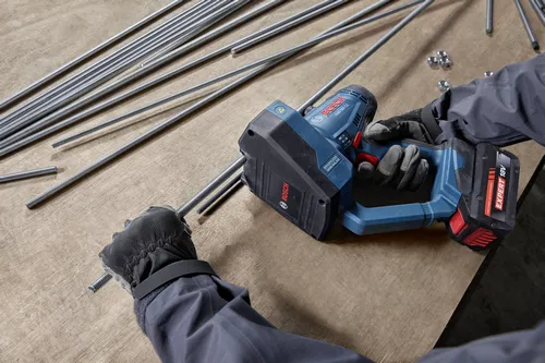 A worker is using a Bosch GGC18V-12 18V Brushless Threaded Rod Cutter to cut threaded metal rods on a workbench.