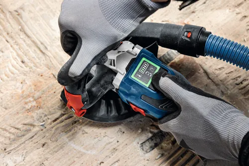 The close-up image of worker using the Bosch GBR18V-15S 5 In. 18V Concrete Surface Grinder to grind a hard concrete floor.