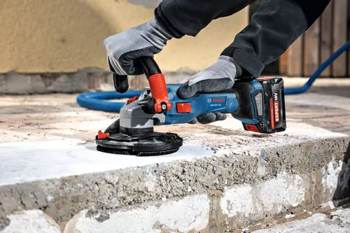 The close-up image of worker using the Bosch GBR18V-15S 5 In. 18V Concrete Surface Grinder to grind a hard concrete floor.